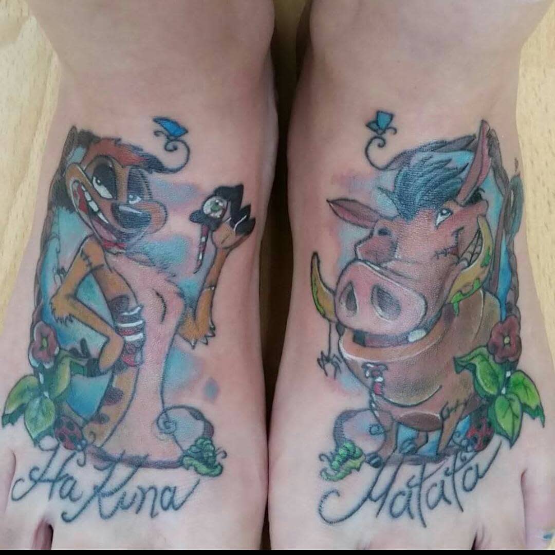 Tattoos of Timon and Pumbaa on feet with "Hakuna" and "Matata" text and colorful flowers
